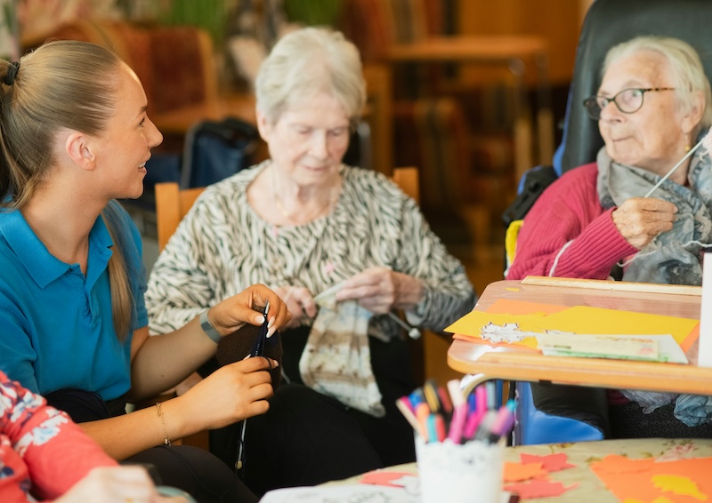 female residents sat down doing arts and crafts while talking to an activities assistant